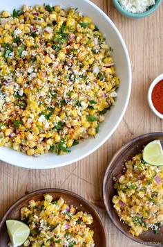 two bowls filled with mexican street corn next to some spices and seasoning on the table