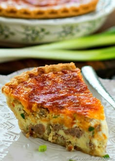 a piece of quiche on a plate with a fork and bowl in the background