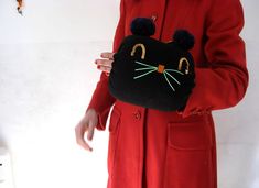 a woman in a red coat holding a black cat purse