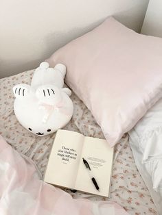 an open book on a bed next to a stuffed animal with a pillow and pen