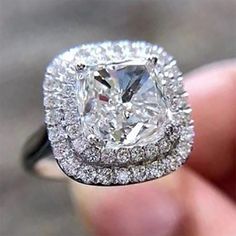 a close up of a person's hand holding a ring with a large diamond in it