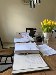 a wooden table topped with notebooks and yellow flowers next to a vase filled with tulips