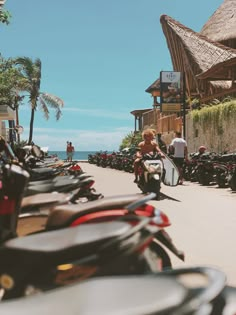 motorcycles parked on the side of a road next to some palm trees and people walking