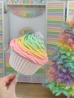 a person holding a cupcake with rainbow frosting on it in front of a christmas tree