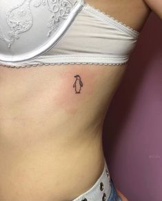 a small penguin tattoo on the side of a woman's stomach is seen in this image