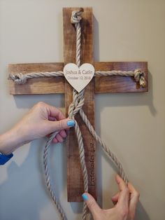 two hands holding a cross with a heart on it and rope attached to the wall