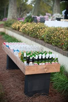 several bottles of beer are lined up on a wooden bench in front of some bushes