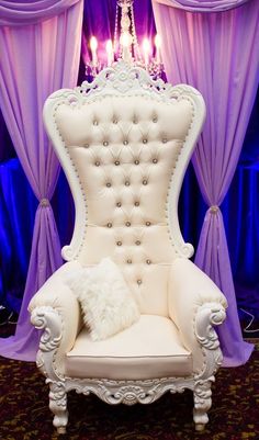 a white chair with a pillow on top of it in front of purple drapes