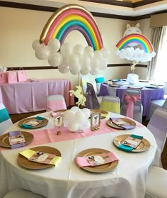 a table set up for a baby shower with balloons and rainbows in the background