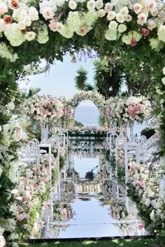 an outdoor ceremony with white and pink flowers on the aisle, surrounded by greenery