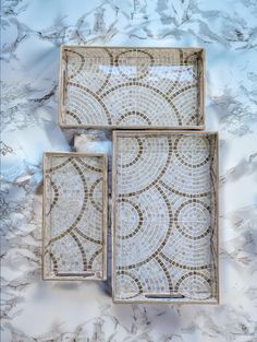 three square trays with decorative designs on them sitting on a marble countertop top