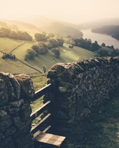 a wooden bench sitting on the side of a stone wall next to a lush green field