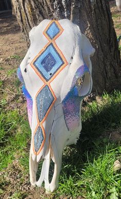 a cow skull is sitting in the grass next to a tree with an intricate design on it's head