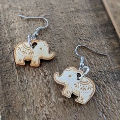 two silver and gold elephant earrings sitting on top of a wooden table