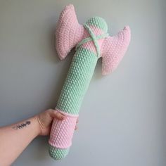 a hand holding a pink and green knitted object on a gray surface with writing underneath it