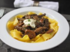 a white bowl filled with pasta and meat covered in sauce on top of a table