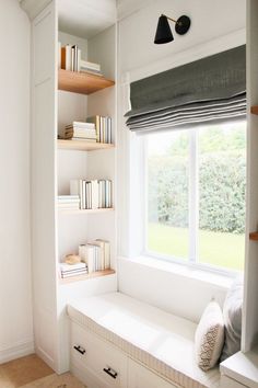 there is a window seat in the corner of this room with some books on it