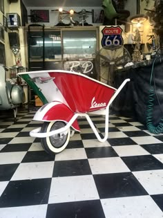 a red and white wheelbarrow sitting on top of a checkered floor