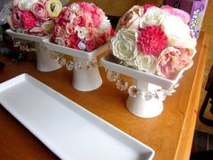 three white vases with flowers in them sitting on a table next to a plate