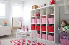 a child's playroom with pink bins and white shelving unit filled with toys