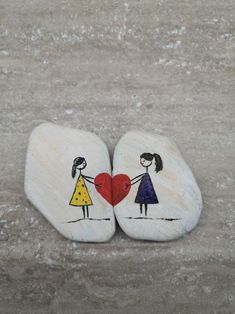 two painted rocks with children holding hands and a heart on them, sitting next to each other