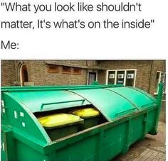 a green dumpster sitting on the side of a road next to a brick building