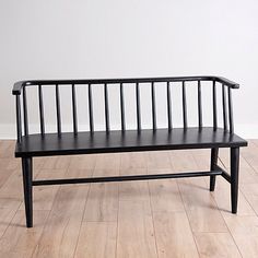 a black bench sitting on top of a hard wood floor next to a white wall