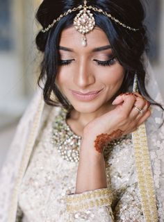 a woman wearing a white and gold bridal outfit with her hands on her chest