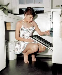 a woman is opening the oven door and looking at something on the floor in front of her