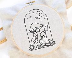 an embroidery project with a mushroom and mushrooms in the night sky, on top of a white