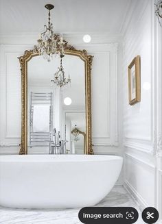 a large white bath tub sitting in a bathroom next to a tall gold framed mirror