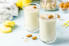 two glasses filled with smoothie next to bananas and almonds on a table top