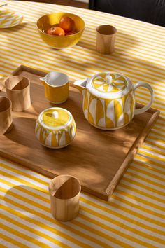 a wooden tray topped with yellow and white dishes next to bowls filled with oranges