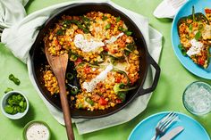 a skillet filled with food on top of a green table next to plates and utensils