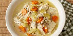 a white bowl filled with chicken and carrots on top of a wooden tablecloth