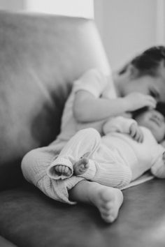 a black and white photo of a baby sleeping on a couch with its mother holding her