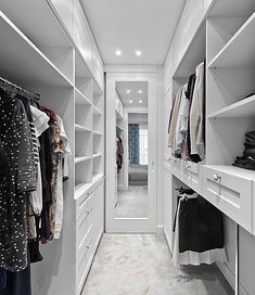 a walk in closet with white shelving and drawers