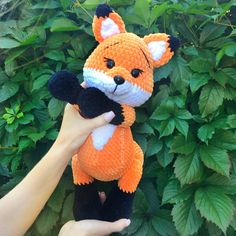 a hand holding an orange and white stuffed animal in front of green plants with leaves