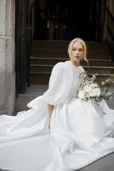 a woman in a white wedding dress sitting on the ground next to some stairs and flowers