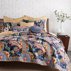 a bed covered in a colorful comforter next to a white brick wall