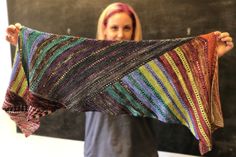 a woman holding up a multicolored shawl in front of a blackboard