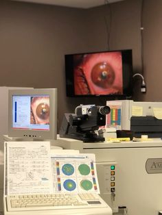 an eye looking through a microscope in front of a computer monitor and laptop on a desk