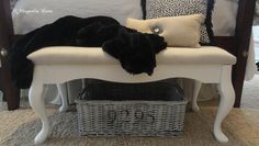 a black cat sleeping on top of a white bench next to pillows and a basket