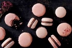 pink macaroons and cookies on a black surface next to a dried purple flower