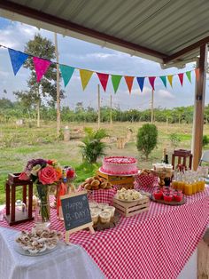 a picnic table with food on it and bunting strung from the roof, in front of an open field