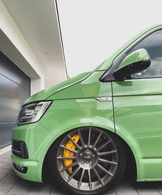 a green van parked in front of a garage door with yellow rims on it