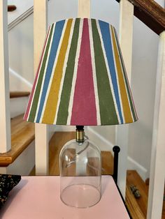 a lamp that is sitting on top of a table next to a stair case in a house