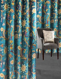 a chair sitting in front of a window covered in blue and yellow curtains with floral designs