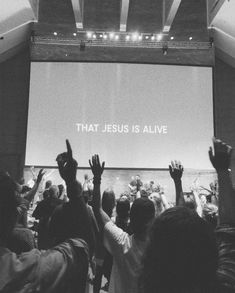 people raising their hands in front of a large screen with the words that jesus is alive on it