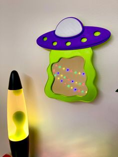 a green and purple alien shaped clock next to a black marker on a white wall